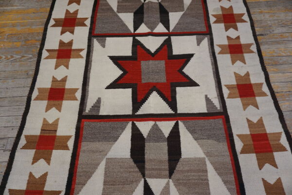 Red, gray, and cream geometric runner rug with a stepped star pattern lies on distressed wood planks.