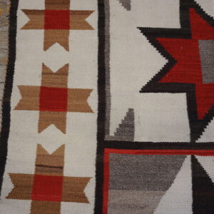 Close detail of a geometric flatweave rug in white, red, tan, black, and gray on weathered wood planks.