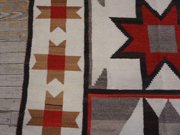 Close detail of a geometric flatweave rug in white, red, tan, black, and gray on weathered wood planks.