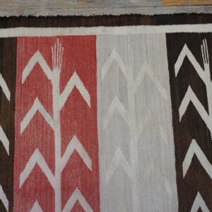 Flat-weave rug with white corn stalk patterns on bold brown, red, and cream vertical stripes.