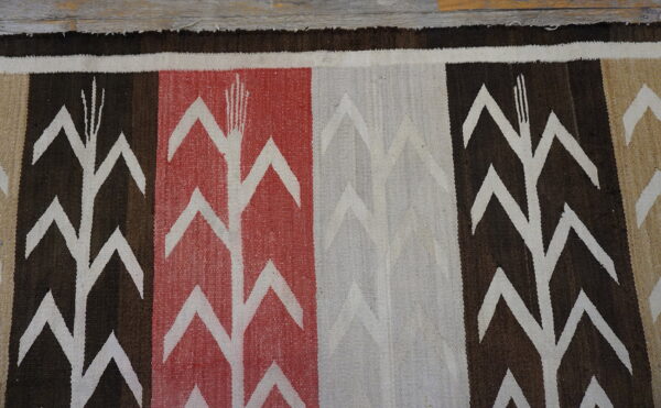 Flat-weave rug with white corn stalk patterns on bold brown, red, and cream vertical stripes.