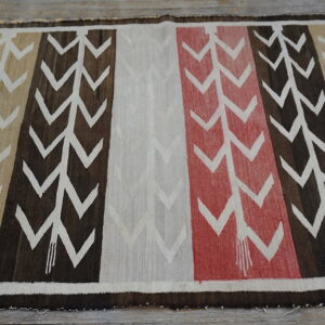 Rug with vertical stripes in tan, brown, off-white, and red chevron patterns laid on wood floor.