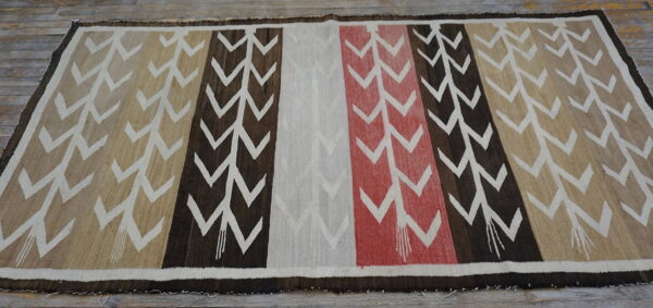 Rug with vertical stripes in tan, brown, off-white, and red chevron patterns laid on wood floor.