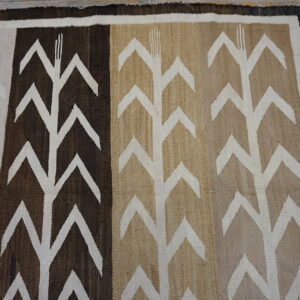 Low-pile rug in brown, tan, and white with large chevron patterns lying on gray wooden floorboards.