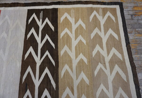 Low-pile rug in brown, tan, and white with large chevron patterns lying on gray wooden floorboards.