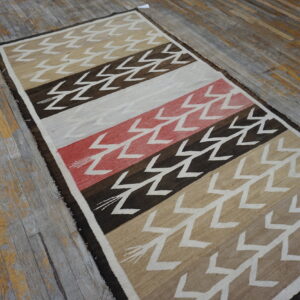 Low-pile striped rug with white zigzag patterns in brown, beige, and red on worn wood floors.