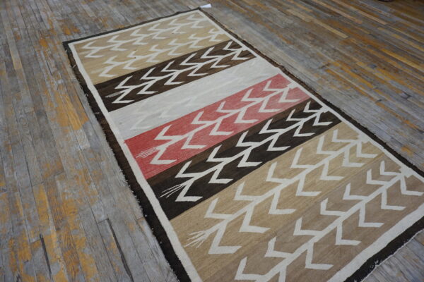Low-pile striped rug with white zigzag patterns in brown, beige, and red on worn wood floors.