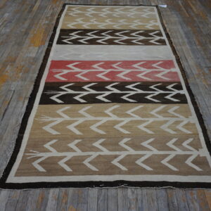 Geometric runner rug featuring chevron patterns in brown, tan, cream, and coral, resting on distressed wood floors.