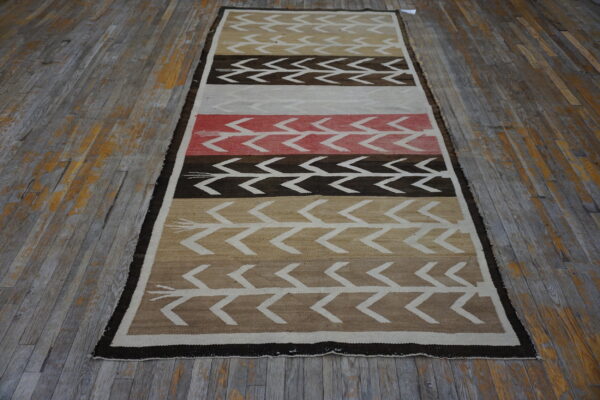 Geometric runner rug featuring chevron patterns in brown, tan, cream, and coral, resting on distressed wood floors.