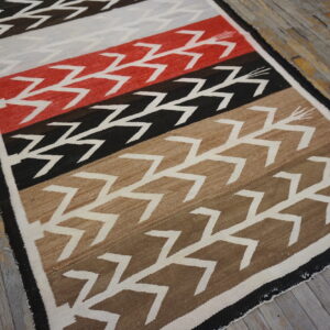 Geometric flatweave rug in red, black, tan, and gray colors with white zigzag motifs on wood planks.