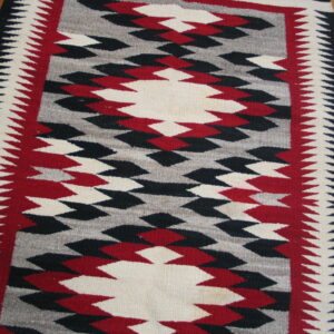 Flatweave rug in red, black, gray, and off-white geometric pattern with sawtooth borders on wood floor.