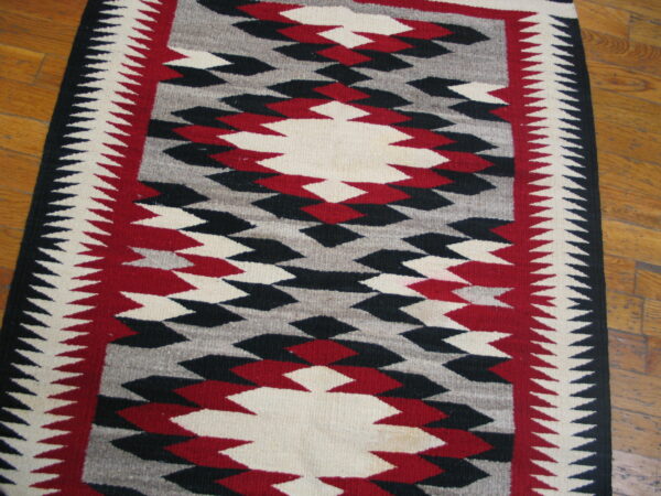 Flatweave rug in red, black, gray, and off-white geometric pattern with sawtooth borders on wood floor.