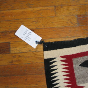 Geometric flatwoven rug in black, red, cream, and gray patterns lies across glossy wood planks.