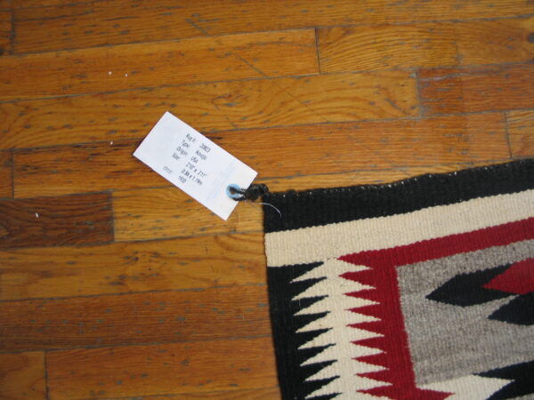 Geometric flatwoven rug in black, red, cream, and gray patterns lies across glossy wood planks.