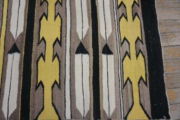 Yellow, brown, black, and cream flatweave rug with serrated patterns lying on distressed wood floor.