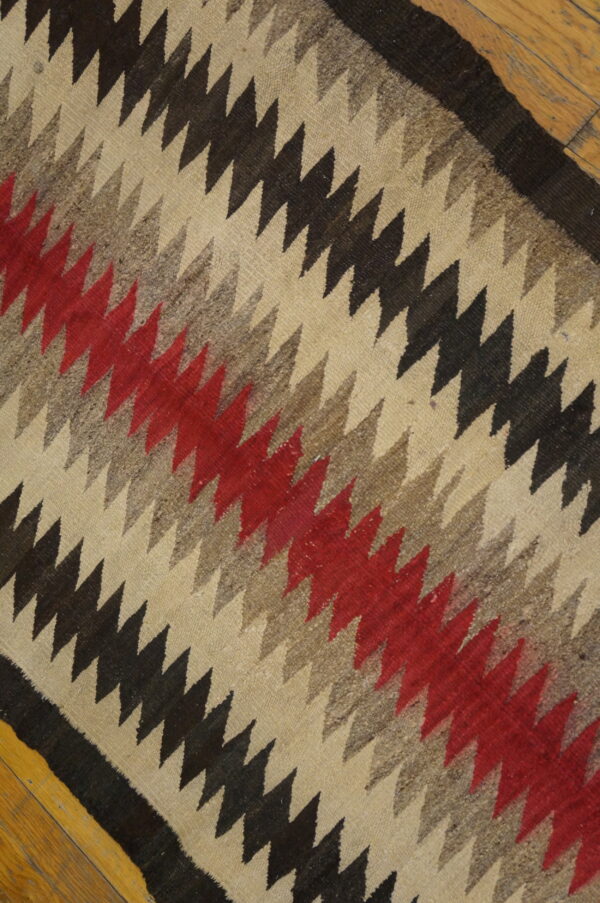 Diagonal zig-zag patterned flatweave rug in cream, black, gray, and red, on hardwood flooring.