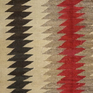 Close-up of a textured rug with vertical zigzag stripes in black, gray, red, and cream next to wood flooring.