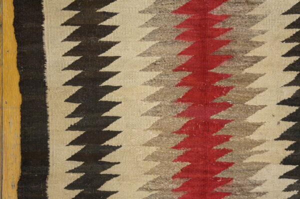 Close-up of a textured rug with vertical zigzag stripes in black, gray, red, and cream next to wood flooring.