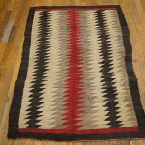 Red, beige, and dark brown zigzag patterned flatweave rug displayed on wooden floorboards.