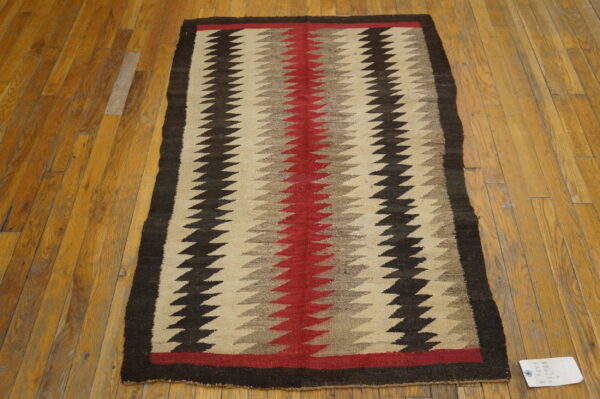 Red, beige, and dark brown zigzag patterned flatweave rug displayed on wooden floorboards.