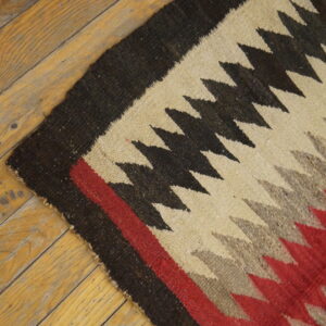 Flat-weave rug with zigzag patterns in black, cream, red, and gray lies on worn wood planks.