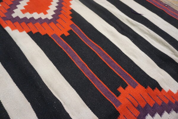 Geometric flatweave rug with bold black, off-white, orange, and purple stripes and stepped motifs.