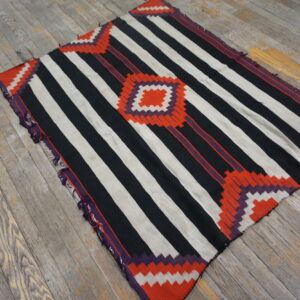 Black and white striped flatweave rug with orange and purple zigzag geometry resting on distressed wood.