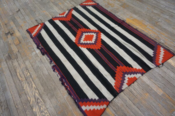 Black and white striped flatweave rug with orange and purple zigzag geometry resting on distressed wood.