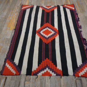 Black and white striped flatweave rug featuring red and purple geometric diamond patterns on distressed wood flooring.