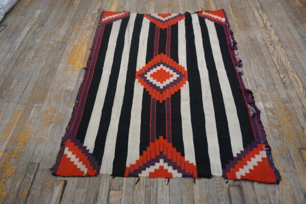 Black and white striped flatweave rug featuring red and purple geometric diamond patterns on distressed wood flooring.
