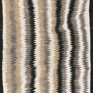A flat-woven rug featuring vertical zigzag stripes in cream, tan, grey, and black colors.