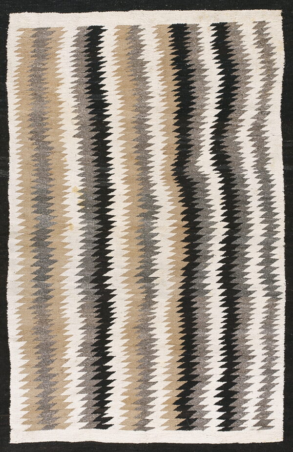 A flat-woven rug featuring vertical zigzag stripes in cream, tan, grey, and black colors.