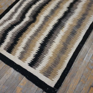 Low-pile rug featuring wide black, cream, and earth-toned zigzag stripes on rustic wooden planks.