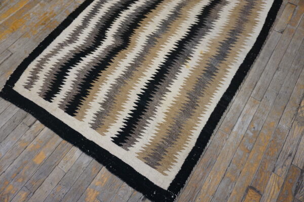Low-pile rug featuring wide black, cream, and earth-toned zigzag stripes on rustic wooden planks.