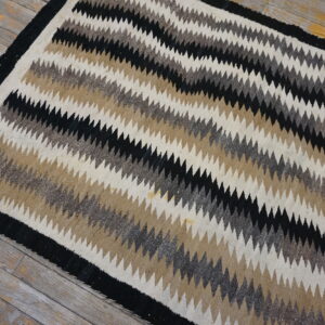 Low-pile rug with diagonal black, brown, gray, and cream zig-zag stripes on weathered wood planks.