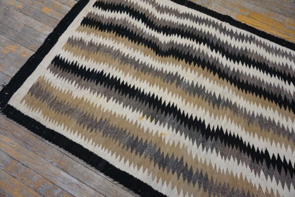 Low-pile rug with diagonal black, brown, gray, and cream zig-zag stripes on weathered wood planks.