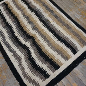 Flatweave rug with black, cream, tan, and gray serrated stripes rests on rustic plank flooring.