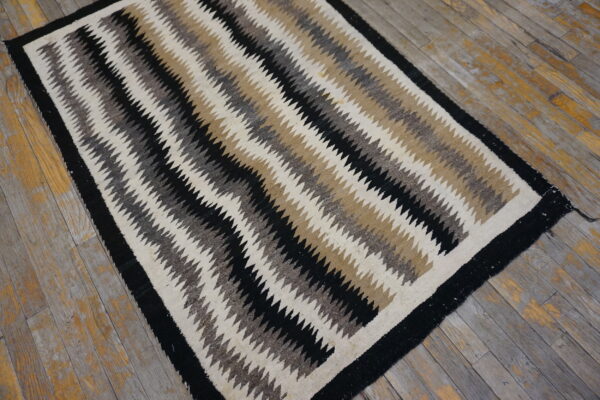 Flatweave rug with black, cream, tan, and gray serrated stripes rests on rustic plank flooring.