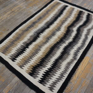 Low-pile rug featuring bold black, beige, gray, and white vertical zigzags on weathered wood.