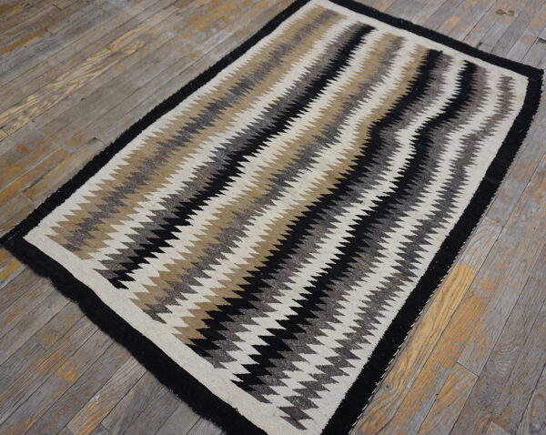 Low-pile rug featuring bold black, beige, gray, and white vertical zigzags on weathered wood.