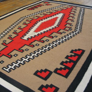 Flat woven rug in tan, red, black, and white geometric patterns on wood flooring.