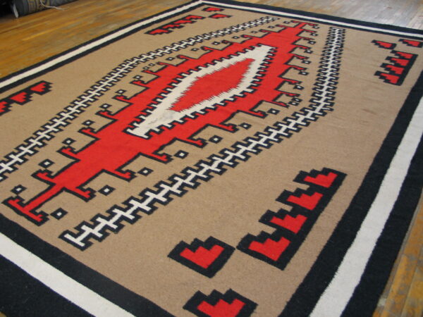 Flat woven rug in tan, red, black, and white geometric patterns on wood flooring.