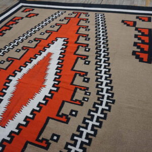 Low-pile rug featuring orange, tan, black, and white geometric stepped patterns on rustic wood flooring.