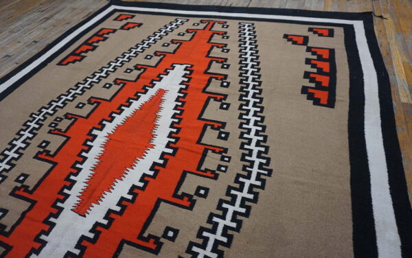 Low-pile rug featuring orange, tan, black, and white geometric stepped patterns on rustic wood flooring.