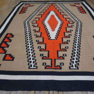 Flat-woven rug with geometric orange, black, and white patterns on a tan background, on a wood floor.