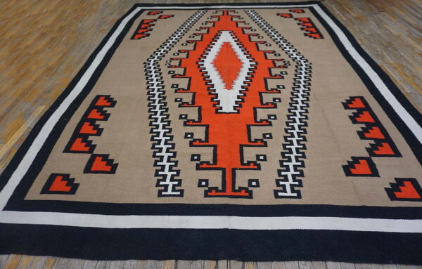 Flat-woven rug with geometric orange, black, and white patterns on a tan background, on a wood floor.