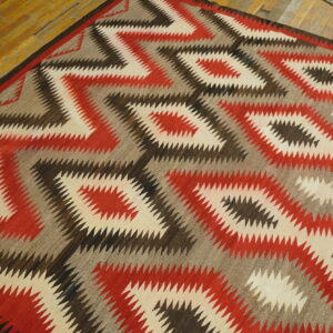 Geometric rug with sharp zigzag diamonds in cream, red, gray, and brown on wood flooring.