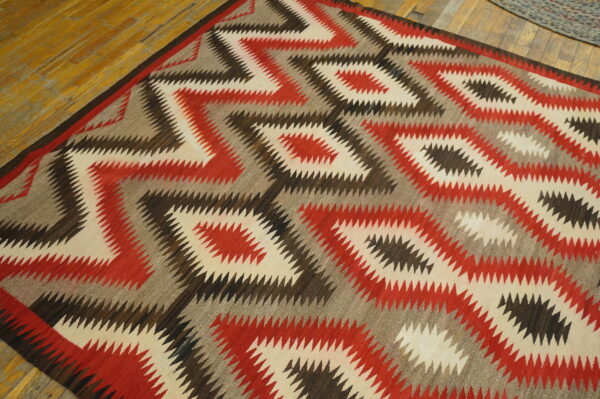 Geometric rug with sharp zigzag diamonds in cream, red, gray, and brown on wood flooring.