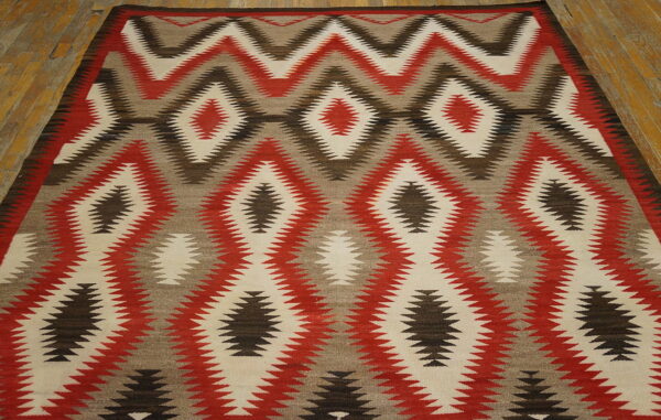 Low pile rug featuring large red, cream, and brown zigzag diamond patterns on distressed wood flooring.