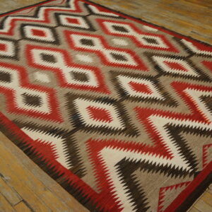 Flatweave rug with red, cream, brown, and taupe zigzag diamond pattern on distressed wood flooring.